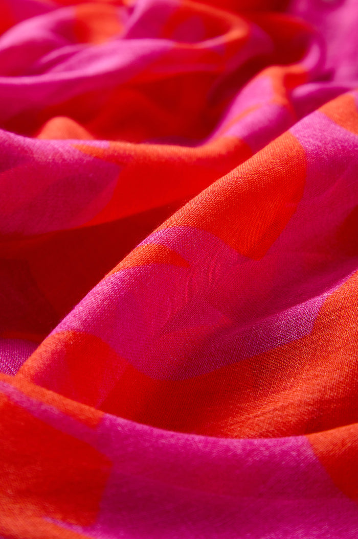 Close-up of the Palm Mirage Scarf in a red and pink modal silk blend, featuring a soft, wavy texture and subtle geometric patterns.