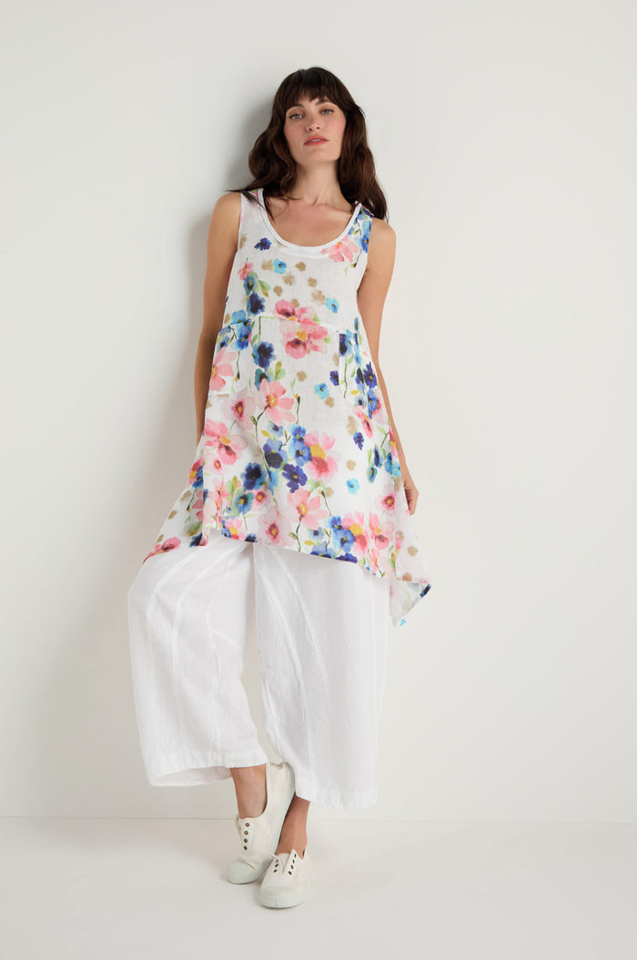A person wears the Primrose Print Sleeveless Linen Tunic over loose white pants and white sneakers, standing against a plain white background.