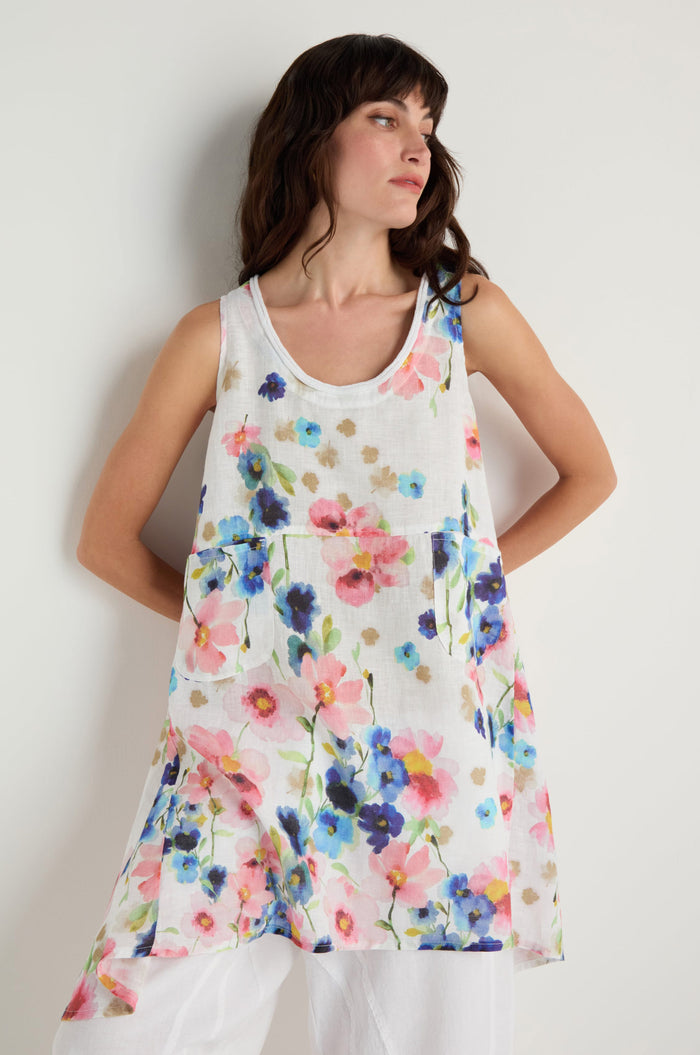 A woman models the Primrose Print Sleeveless Linen Tunic, featuring a loose fit and vibrant floral pattern, set against a simple light background.