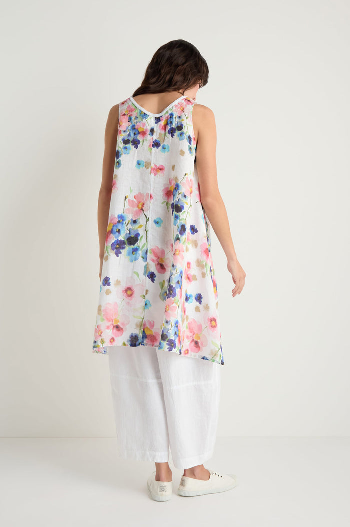 A woman is seen from behind wearing the Primrose Print Sleeveless Linen Tunic over wide white pants and white sneakers, set against a plain white background.