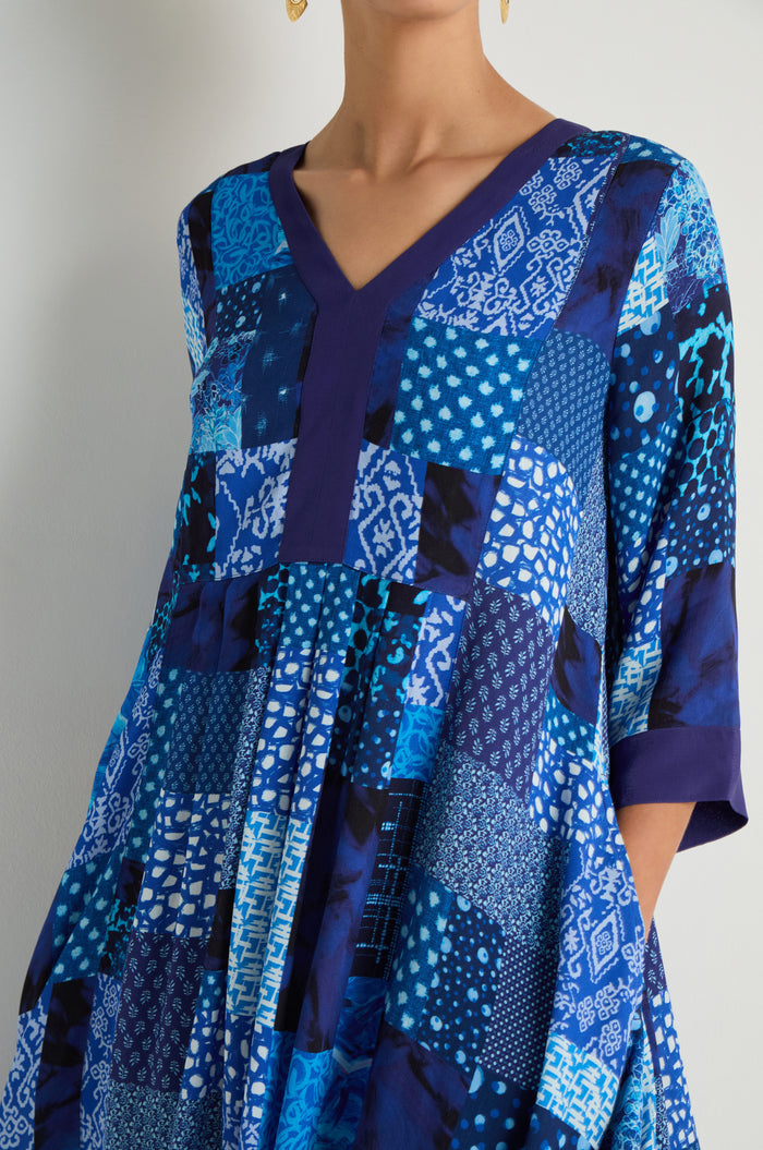 A woman wears the Sahara Indigo Patchwork Flared Dress, featuring three-quarter sleeves, a flared silhouette, and blue geometric and abstract designs on viscose crepe.