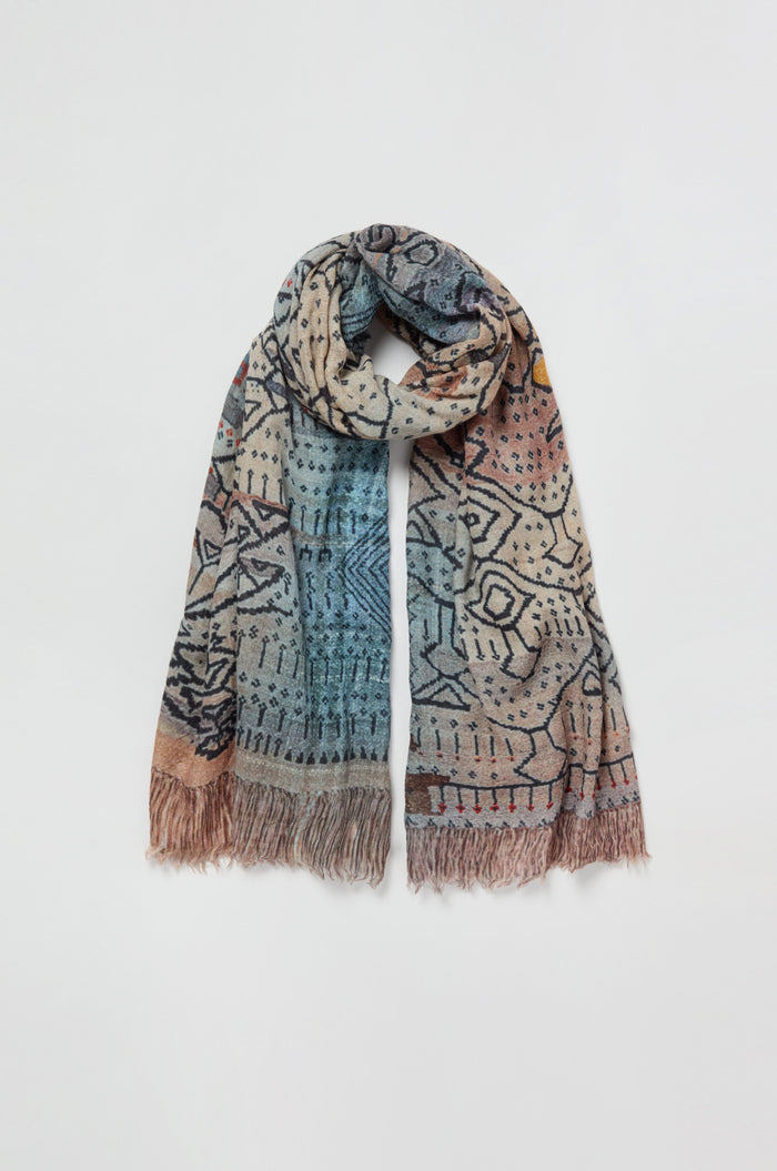 The Sketch Mountain Wool Scarf is a lightweight wool accessory showcasing geometric and abstract print designs in blue, beige, and brown tones, accented with fringed ends and displayed laid flat against a white background.