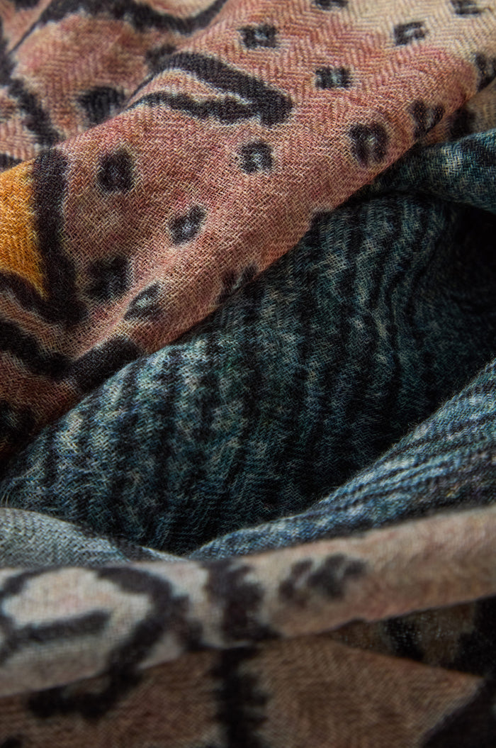 Close-up of the Sketch Mountain Wool Scarf, a lightweight accessory layered with abstract patterns in earthy tones—brown, orange, black, and blue—that highlight its varied textures and unique designs.