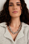 Woman with wavy dark hair wears a textured light-colored jacket and the bold Soft Loops Necklace, looking directly at the camera.