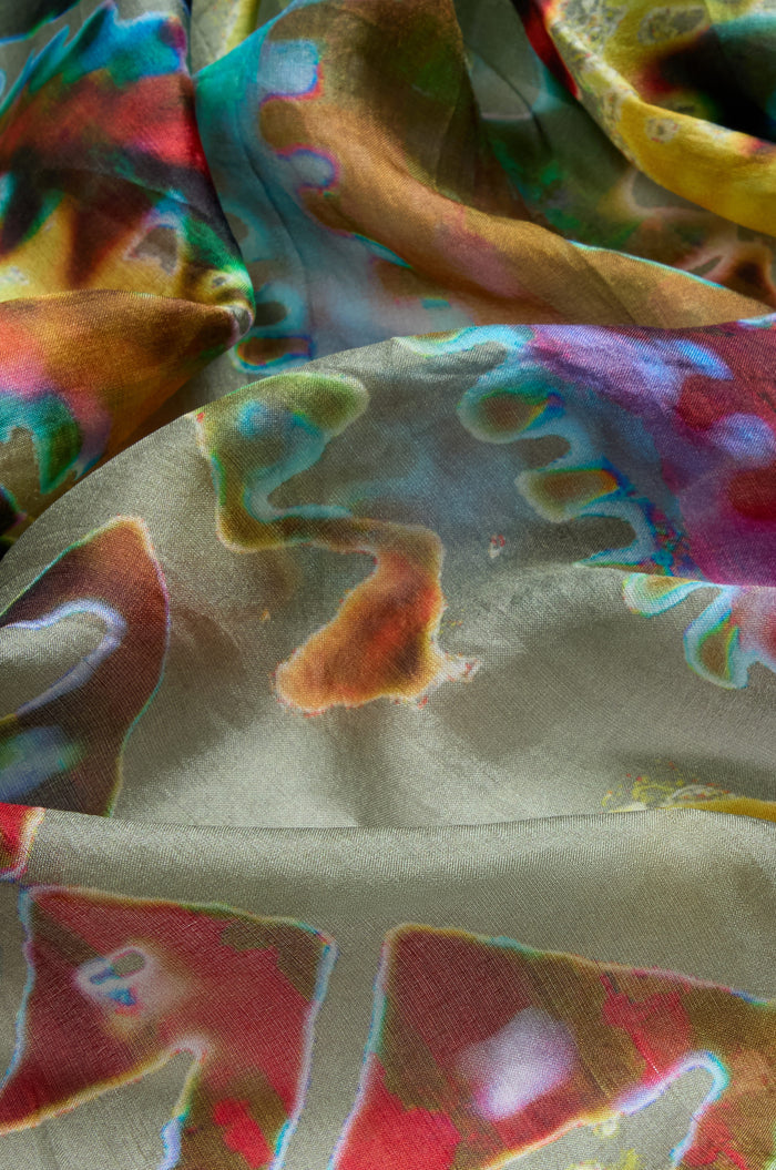 A close-up of the Stained Glass Silk Scarf, crumpled to highlight its multicolored abstract design with wavy green, red, blue, and yellow patterns reminiscent of stained glass.