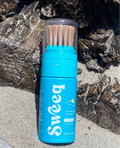 Front view of Sweeq Beach Sand Remover showcasing wooden bristles and blue bottle on a rocky beach surface