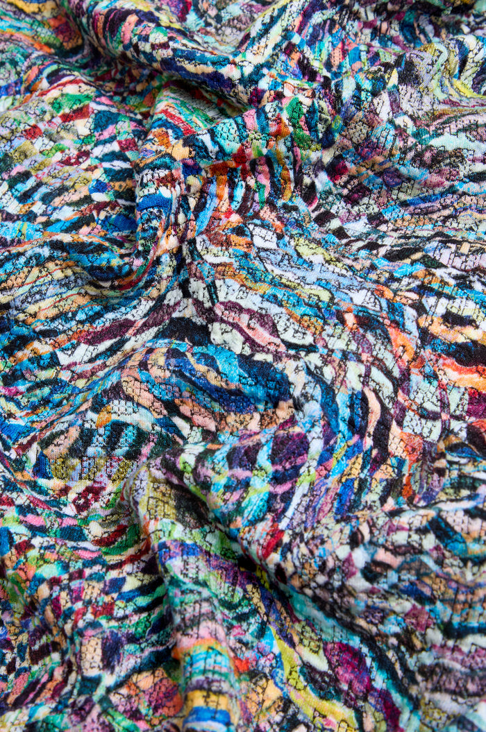 Close-up of crumpled fabric from a Patchwork Fields Jersey Bubble Dress, showcasing a colorful, abstract, multicolored pattern with swirling lines and overlapping shapes.