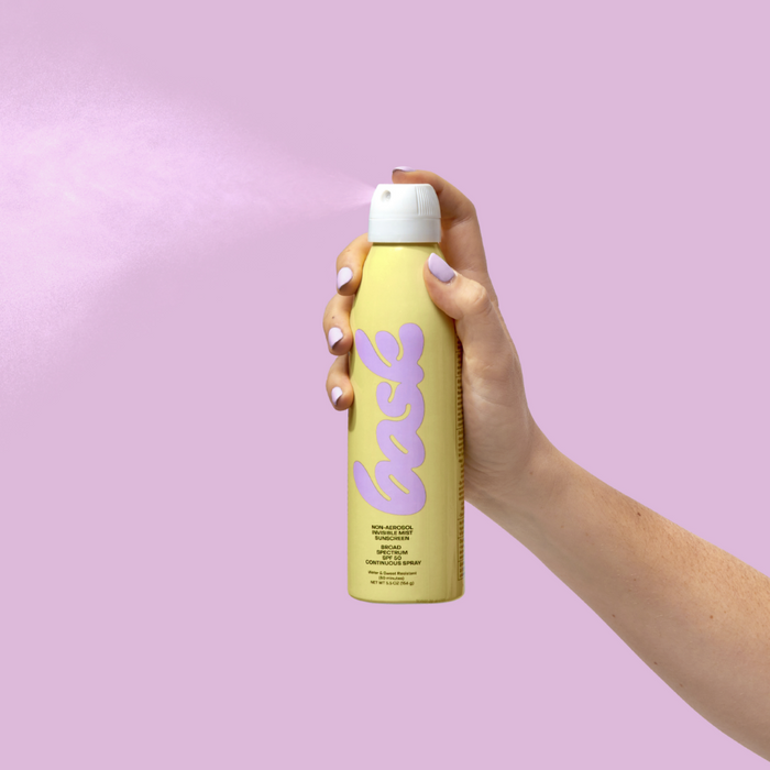 Hand holding a yellow sunscreen bask spray can against a pink background
