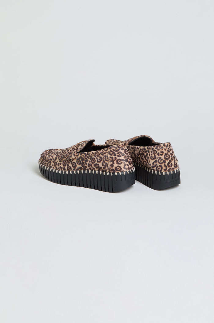 Tulip Leopard Penny Loafers, a pair of slip-on shoes featuring a brown and black leopard print pattern and thick black ridged wedge sole, are positioned on a plain white background.